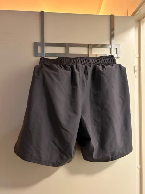 Under Armour - Säljer ett par svarta träningsshorts från Under Armour i storlek S. De har elastisk midja och ett stilrent tryck med loggan längs benet. Materialet är lätt polyester som andas bra och passar perfekt för gym eller löpning. Använda en gång och inte mer då de inte passade mig.