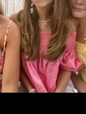 Rosa offshoulder blus från Zara - Säljer en söt rosa offshoulder blus från Zara i storlek S. Blusen har puffiga korta ärmar och smock upptill som ger en snygg passform. Croppad modell med luftig känsla, perfekt för varma dagar. Materialet är lätt och känns skönt mot huden.