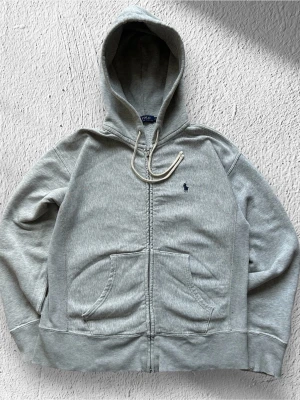 Grå Ralph Lauren Zip Hoodie - Klassisk Ralph Lauren hoodie i grå färg. Tröjan är i bra skick men eftersom den är några år gammal så är dragkedjan lite seg (men den funkar fortfarande bra) samt den är lite ”lös” vid ändarna av ärmarna och midjan men inget som syns tydligt.  Storlek: S Skick: Bra skick! Har lite syn på användning (läs vad jag skrev ovan) Färg: grå Märke: Ralph Lauren Modell: Hoodie med dragkedja   Hör gärna av dig vid frågor så svarar jag så fort jag kan! 😁