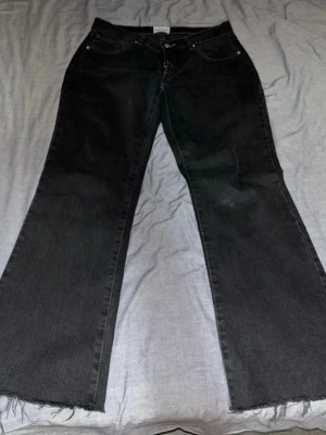 Svarta bootcut jeans från Abrand - Säljer ett par svarta jeans från Abrand, modell A '99 Low Boot. De har bootcut-ben med rå kant nertill och klassisk femficksdesign. Jeansen är lågmidjade och tillverkade i jeansmaterial med snygga sömmar och knapp med Abrand-logga.