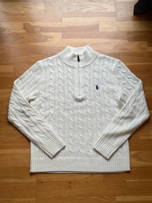 Vit kabelstickad tröja Polo ralph Lauren S - Kabelstickad vit tröja från Polo Ralph Lauren med half zip och hög krage. Klassisk broderad logga på bröstet. Tröjan är långärmad och har ribbade muddar samt nederkant. Perfekt för kyliga dagar och riktigt snygg till jeans.