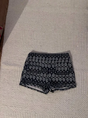 Blå mönstrade shorts med vit print - Säljer ett par blå shorts med vitt blommigt och geometriskt mönster. De har en tight passform och är midwaist. Materialet känns som bomull och de är perfekta för varma sommardagar. Snygga att matcha med en enkel topp eller hoodie.