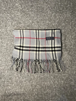 Burberry Halsduk Grå - Klassisk Burberry-halsduk i 100 % lammull. Mjuk och varm med tidlöst rutmönster i grått, svart, vitt och rött. Originaletikett, Made in England. 2G