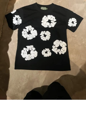 Svart t-shirt med vita blommor - Cool svart t-shirt med stora vita blommor tryckta över hela plagget, både fram och bak. T-shirten har klassisk passform och rund hals. Perfekt för dig som vill sticka ut med ett unikt mönster.