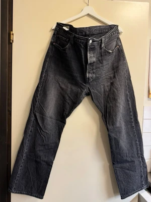  Levi's 501  - Säljer ett par svarta raka jeans från Levi's med klassisk femficksdesign och knappgylf. Jeansen har en avslappnad passform och är tillverkade i slitstark denim. Perfekta för dig som gillar en tidlös och cool stil.