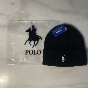 Svart ribbstickad mössa Polo Ralph Lauren - Säljer en svart ribbstickad mössa från Polo Ralph Lauren med den klassiska broderade loggan i vitt framtill. Mössan har uppvikt kant och är tillverkad i mjukt material som håller dig varm och snygg under kalla dagar.