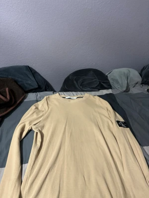  tröja Calvin Klein - Säljer en beige långärmad tröja från Calvin Klein Jeans i storlek XL. Tröjan har en rund halsringning och är tillverkad i ett strukturerat, waffle-liknande material. Perfekt för dig som gillar stilrena och enkla plagg. Storlek xl.