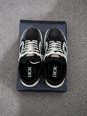 Svarta Dior b30  - Säljer ett par snygga Dior sneakers i svart med vita och grå detaljer. Skorna har en chunky sula, vita snören och meshpartier för extra komfort. Märkeslogga på plösen och insidan. Perfekta för dig som vill ha en exklusiv och trendig look.