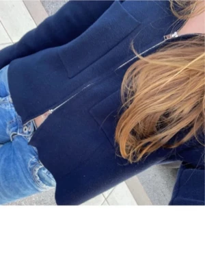 Mörkblå zip-jacka med fickor - Snygg mörkblå jacka med dragkedja framtill och två stora fickor. Jackan har en enkel och stilren design, perfekt att slänga på sig över en t-shirt. Materialet ser ut att vara mjukt och lite tjockare, vilket gör den skön att bära under kyligare dagar.