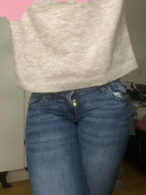 Low waist bootcut jean - Säljer ett par mörkblå bootcut jeans med klassisk femficksdesign och guldfärgad dragkedja. Jeansen har en lätt tvättad look och sitter tajt upptill med utsvängda ben. Lågmidjade och är i fint skick, finns lite slutningar där nere men inget man märker