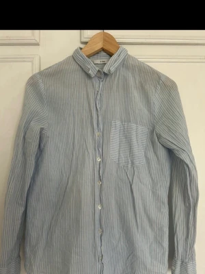 Blåvit randig skjorta DF Young - Snygg blåvit randig skjorta från DF Young i storlek S. Skjortan har klassisk krage, lång ärm och en bröstficka med horisontella ränder. Tillverkad i mjuk bomull och stängs med knappar framtill.