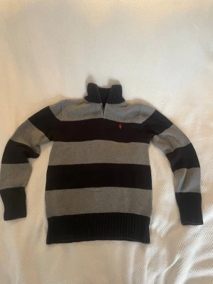 Ralph Lauren tröja - Riktigt fet stickad tröja med breda svarta och grå ränder från Ralph Lauren. Tröjan har halv dragkedja, hög krage och ribbade muddar. Varm och väldigt skön när det är kallt ute. Passar XS och kan även passa S
