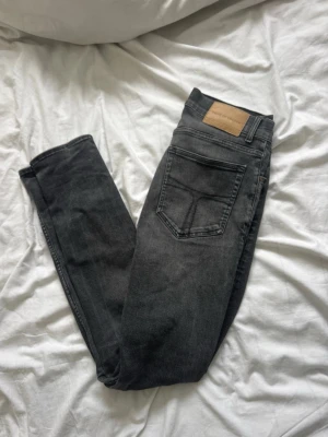 Svarta jeans från Tiger of Sweden - Snygga svarta jeans från Tiger of Sweden med klassisk femficksdesign och läderpatch bak i midjan. Jeansen har smal passform och är tillverkade i stretchigt denim för en bekväm känsla. Perfekta till en trendig vardagslook.