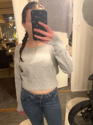 Ljusgrå off shoulder stickad tröja - Säljer en ljusgrå stickad tröja med off shoulder-design och långa ärmar. Tröjan är croppad och har ribbstickade muddar vid ärmslut och nederkant. Perfekt för dig som gillar en avslappnad och trendig stil. Materialet känns mjukt och bekvämt mot huden.