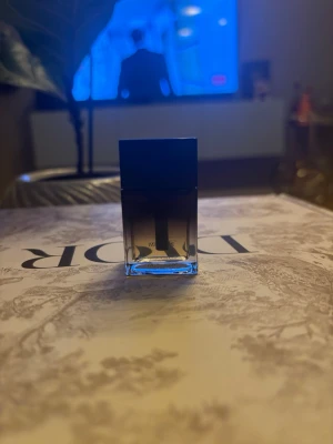 Dior Homme parfymflaska 10 ml - Snygg parfymflaska från Dior Homme med stilren design. Flaskan är rektangulär i glas med en mörk överdel och transparent nederdel som visar vätskan. Märkets logga syns tydligt på framsidan. Perfekt för dig som gillar exklusiva dofter. Innehåller 10 ml och är resestorlek. 