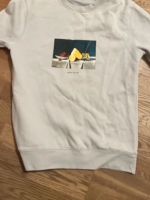 Vit sweatshirt från Poetic Collective - Vit sweatshirt från Poetic Collective med tryck av ett konstmotiv på bröstet. Tröjan har rund halsringning och ribbade muddar vid ärmslut och nederkant. Perfekt för dig som gillar streetwear och konstnärliga detaljer.