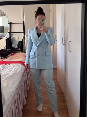 Ljusblå dubbelknäppt kavaj och byxor från Zara - Snygg ljusblå kavaj från Zara med dubbelknäppning och markerade axlar. Kavajen har två fickor framtill och breda slag. Perfekt för en trendig och stilren look. Materialet är slätt och ger en dressad känsla. Kavaj och byxor är xs. Jag är 160 så jag tror inte att byxor kommer passa om man är längre, bara om man vill att de ska vara korta såklart. Använd sparsam.  