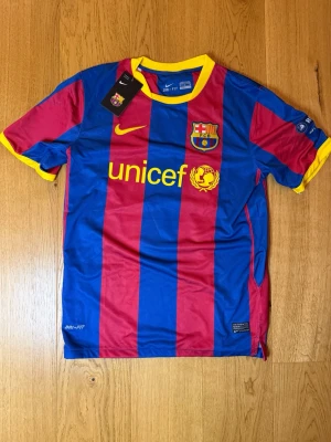 FC Barcelona Messi matchtröja - Säljer en officiell FC Barcelona matchtröja från Nike med Messi och nummer 10 på ryggen. Tröjan har blå och röda vertikala ränder, gula detaljer och klubbmärke på bröstet. Tillverkad i lätt och ventilerande Dri-FIT material, perfekt för fotboll eller träning.