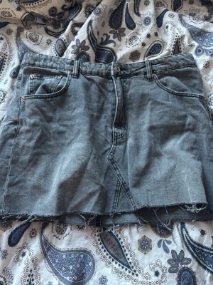 Grå jeanskjol med rå kant - Grå jeanskjol i kort modell med rå, fransig kant nertill. Klassisk femficksdesign och dragkedja framtill. Perfekt för en avslappnad och trendig look.