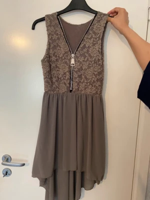 Klänning med spets och dragkedja - En snygg brun/gråish klänning. Kort framtill och längre bakdel. Storlek S/XS