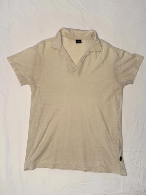Beige kortärmad piké från BOSS - Snygg beige linnepiké från BOSS med korta ärmar och klassisk krage. Tillverkad i mjukt material som känns skönt mot huden. Perfekt för en avslappnad men stilren look. OBS finns litet hål.