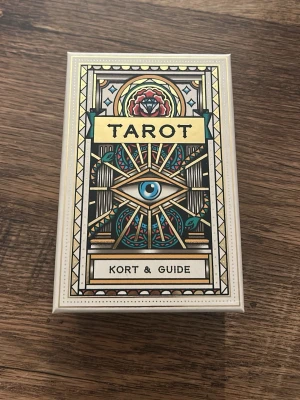 Tarotkort med guidebok - Tarotkortlek med snyggt illustrerade kort och tillhörande guidebok på svenska. Lådan har ett öga och geometriska mönster i färger som guld, blått och rött. Perfekt för dig som vill utforska tarot och spådom.
