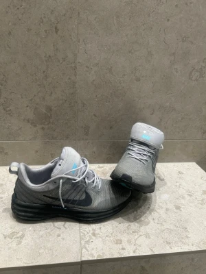 Grå Nike sneakers med svart sula - Snygga grå sneakers från Nike med svart sula och diskret blå logga på plösen. Ovandelen är i meshmaterial för bra andningsförmåga och skorna har klassisk snörning. Perfekta för dig som gillar sportig och clean stil. Ny pris 1200, hos mig 649 där skorna aldrig nästan används. Priset kan sänkas vid snabb affär.