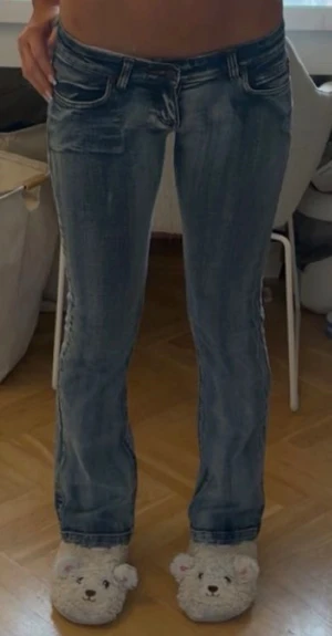 Blå bootcut jeans med slitningar - Säljer ett par blå bootcut jeans med snygga slitningar och tvättade detaljer. Jeansen har låg midja, klassiska fem fickor och raka ben. Perfekta för en avslappnad och trendig look.
