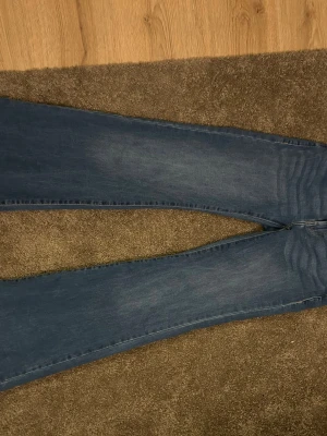 Blå lågmidjade bootcut jeans från Only - Säljer ett par klassiska blå bootcut jeans från Only. Jeansen har en snygg tvättad look, fem fickor och ett brunt läderpatch bak i midjan. Materialet är mjukt denim som sitter skönt och följer kroppen. Lågmidjade!