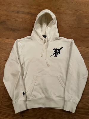 Vit hoodie från Polo Ralph Lauren - Riktigt fet vit hoodie från Polo Ralph Lauren med stor huva och dragsko. På bröstet finns ett mörkblått P-tryck och nere vid ärmen syns den klassiska Polo-loggan. Hoodien har en stor magficka och ribbade muddar. Perfekt för en avslappnad och stilren look. Tröjan är i väldigt bra skick. Hör av er vid minsta fundering😀Pris kan diskuteras.