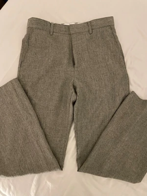 Utavängda grå kostymbyxor - Stilrena grå kostymbyxor med utsvängd passform och pressveck. Byxorna har bälteshällor och stängs med dragkedja och knapp. Perfekta för en dressad look och tillverkade i en mjuk ullblandning. (Storlek 38 men passar som 30)