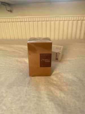 Ombre Notes Eau de Parfum Khadlaj - Ombre Notes Eau de Parfum från Khadlaj i en elegant, fyrkantig förpackning med varm bronsfärg och stilren design. Kartongen har en glansig finish och tydlig märkning framtill. Perfekt för dig som gillar exklusiva dofter och snygg förpackning.Pris kan diskuteras 