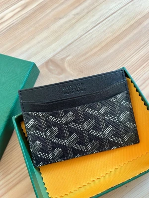 Svart kortfodral från Goy4rd - Snyggt svart kortfodral från Goy4rd med klassiskt mönster i vitt och grått. Tillverkat i läder och canvas, perfekt för kort och sedlar. Kommer i original grön ask med tillhörande tyg och tagg. Stilren och lyxig accessoar för dig som gillar designer.