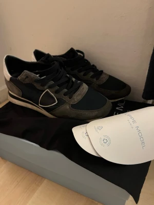 Phillipe model trainers i bra skick! - Säljer dessa riktigt snygga Phillipe model trainers som jag inte användt mycket alls och de är i väldigt fint skick! Allt og följer med! Alltså og box, dustbag, innerskydd. I blått tyg och grå mocka, med riktigt snygga vita detaljer! Snyggaste skorna utan tvekan! Kan tänka mig byten. Lätta att matcha me andra klädesplagg, d mesta blir snyggt ihop me dessa!