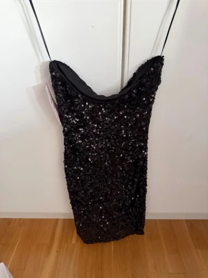 Svart paljettklänning från Nelly - Säljer en svart kort klänning från Nelly (aldrig använd) täckt av glittriga paljetter. Klänningen har en figurnära passform och den har en snygg tubformad design.