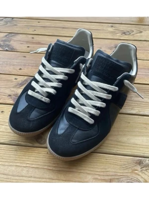 Svarta sneakers från Maison Margiela - Snygga svarta sneakers från Maison Margiela med vita snören och klassisk gummisula. Skorna har en stilren design i mocka och skinn, perfekta för dig som gillar minimalistisk och trendig stil.