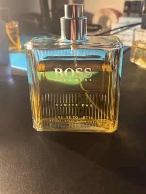 Hugo Boss Number One Eau de Toilette - Klassisk parfym från Hugo Boss i en stilren, fyrkantig glasflaska med silverfärgad spraykork. Doften heter Number One och flaskan har guldfärgad vätska och vita linjer som dekoration. Perfekt för dig som gillar eleganta och tidlösa dofter. 125ml flaska men använd locket har jag tappat bort tyvär 