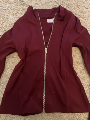 Vinröd zip hoodie från Gina Tricot - Snygg vinröd träningströja från Gina Tricot med dragkedja framtill och hög krage. Tröjan har långa ärmar och är gjord i ett mjukt, stretchigt material. Perfekt för en avslappnad och trendig look. aldrig använd. 