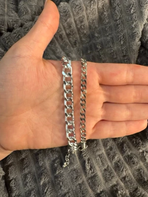 Armband - Säljer två stilrena armband i silverfärg med klassisk kedjedesign. Ena armbandet har bredare länkar medan det andra är smalare, båda med justerbar längd och karbinlås. Perfekta för att mixa och matcha till olika outfits.