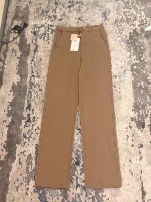 Beige raka kostymbyxor - Snygga beige kostymbyxor med raka ben och hög midja. Byxorna har bälteshällor, sidofickor och stängs med dragkedja och knapp. Perfekta för en clean och stilren look.