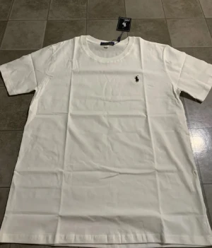 Vit t-shirt från Polo Ralph Lauren XL - Vit t-shirt från Polo Ralph Lauren i klassisk modell med rund hals och korta ärmar. T-shirten har den ikoniska broderade loggan på bröstet och är gjord i mjuk bomull. Perfekt för dig som gillar stilrena och tidlösa plagg med snygg passform.