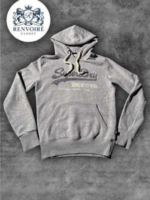 Grå Superdry hoodie med tryck - En riktigt fet och eftertraktad hoodie från superdry med en sällsynt grå färg och runda snören, storlek XS men passar bättre som S Skulle jag säga