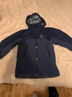 Blå Arc'teryx BETA AR - Säljer en mörkblå Arc'teryx BETA AR i storlek L. Jackan är tillverkad i slitstark Gore-Tex, har huva, flera dragkedjeförsedda fickor och snygg logga på bröstet. Perfekt för dig som vill ha en stilren och funktionell jacka till vardagsäventyr eller ett bra skal till skidåkning.
