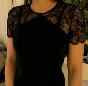 Svart spetsbody från Pieces - Svart body från Pieces med korta ärmar. Toppen har en snygg öppen rygg och är detaljerad i spets! 