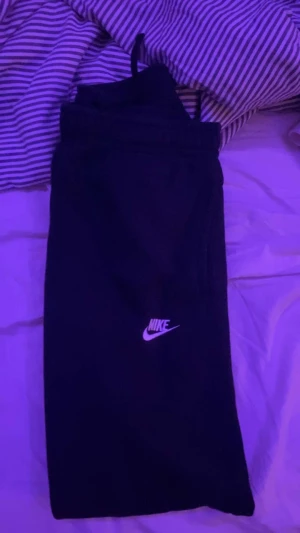 Svarta mjukisbyxor från Nike S - Svarta mjukisbyxor från Nike med klassisk vit logga på benet. Byxorna har elastisk midja med snörning och är tillverkade i mjukt bomullsmaterial. Perfekta för chill eller träning, riktigt sköna och stilrena.