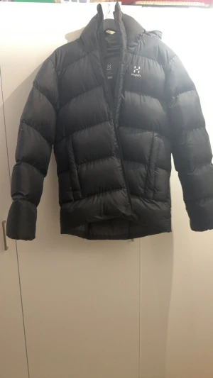 Haglöfs vinterjacka  - Säljer den Haglöfs vinterjackan  som är är jätte skön och varm, men den har gått sönder jätte lite på högra ärmen som ni kan se, men det kan jag lösa genom att sy innan jag fraktar den. I bra skick och använt 1 säsong bara. Köpte den för 2000 men kan tänka mig att sälja den  runt 1500 men vi kan även diskutera om priset.
