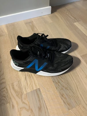 Svarta New Balance 890 sneakers V8 - Ordinarie pris 1400kr. Snygga svarta New Balance 890 sneakers med blått N på sidan och vita detaljer på sulan. Skorna har snörning och är tillverkade i ett lätt syntetmaterial med mesh för bra ventilation. Perfekta för dig som gillar sportig stil och vill ha bekväma skor med cool design.