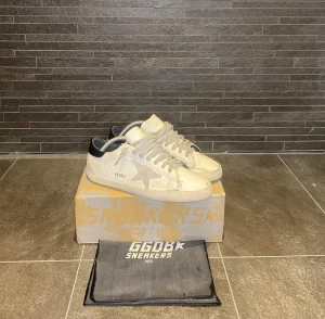 Golden Goose Superstar  - Golden Goose Superstar sneakers i vitt skinn med grå snörning och silverfärgad stjärndetalj på sidan. Nypris på dessa ligger runt 5000kr. Skorna har precis anlänt hem efter en lagning hos skomakeriet vid hålpartierna! Hör av er om frågor eller prisförslag!