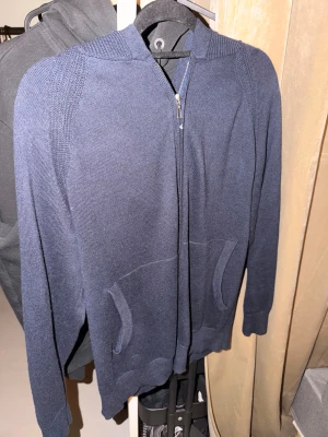 Loro piano kofta - Snygg marinblå stickad hoodie från Los Angeles Lakers med dragkedja framtill och två fickor. Tröjan har huva och ribbade detaljer vid axlar och muddar. Perfekt för dig som gillar sportiga och bekväma plagg med stil.