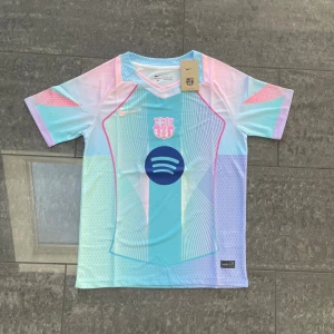 Barcelona Jersey 25/26 - Unik FC Barcelona fotbollströja från Nike i pastellfärger med blå, rosa och ljusgröna toner. Tröjan har korta ärmar, Polyester material och tryckta detaljer som klubbmärke och Spotify-logga. Snyggt geometriskt mönster och exklusiv design.